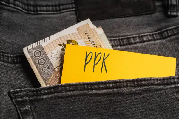 Żółta kartka z napisem "ppk" wystaje z kieszeni dżinsów obok banknotów. Decyzja o rezygnacji z PPK.