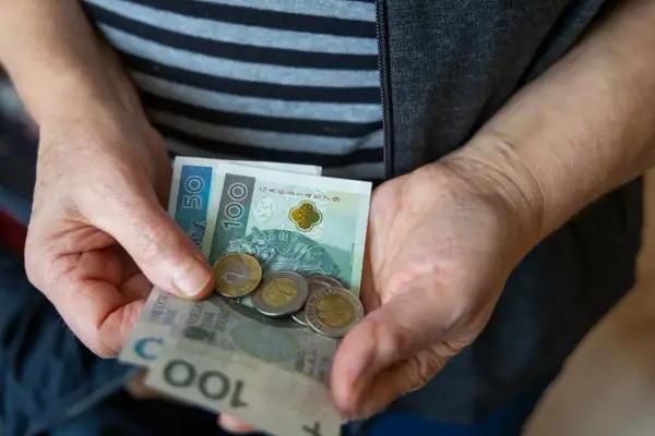 Dłonie trzymają polskie banknoty i monety. Nadzieja na waloryzację rent i emerytur 2026.