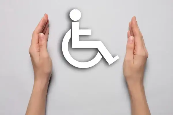 Dwie dłonie otaczają biały symbol osoby na wózku inwalidzkim, symbolizując wsparcie i akceptację dla osób z niepełnosprawnościami.